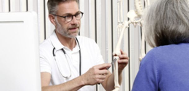 Ein Arzt erklärt einer Patientin an einem Modell-Skelett den Aufbau des Kniegelenks.