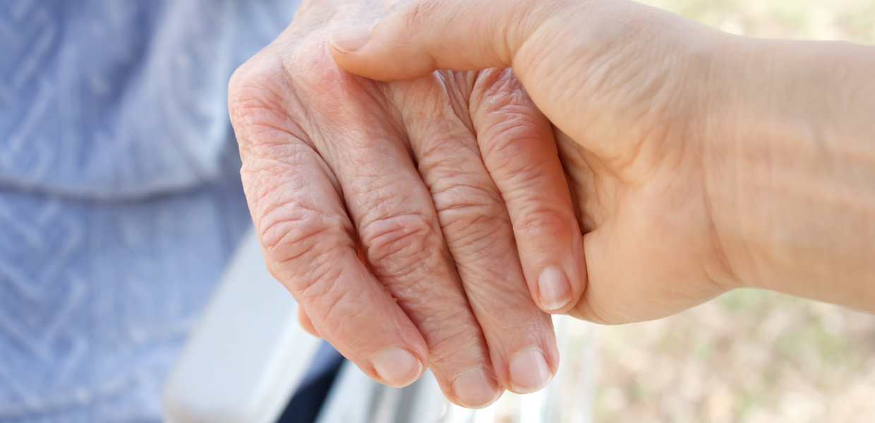 Eine jüngere Frau hält die Hand einer älteren Frau.